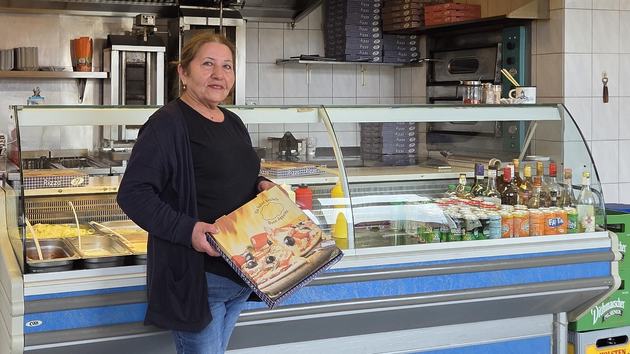 Krümel (Frau Ural) mit einem Pizzakarton in ihrem Grillhaus "Krümel's Grill"- ihre Pizza ist nicht nur im Ort berühmt und beliebt