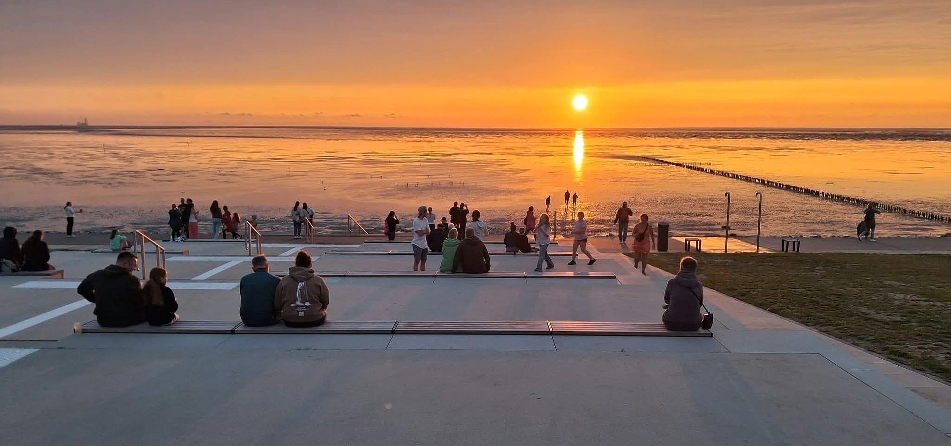 Gut besuchte Tribüne am Trischendiek Strand mit Sonnengang über dem Wattenmeer im Hintergrund